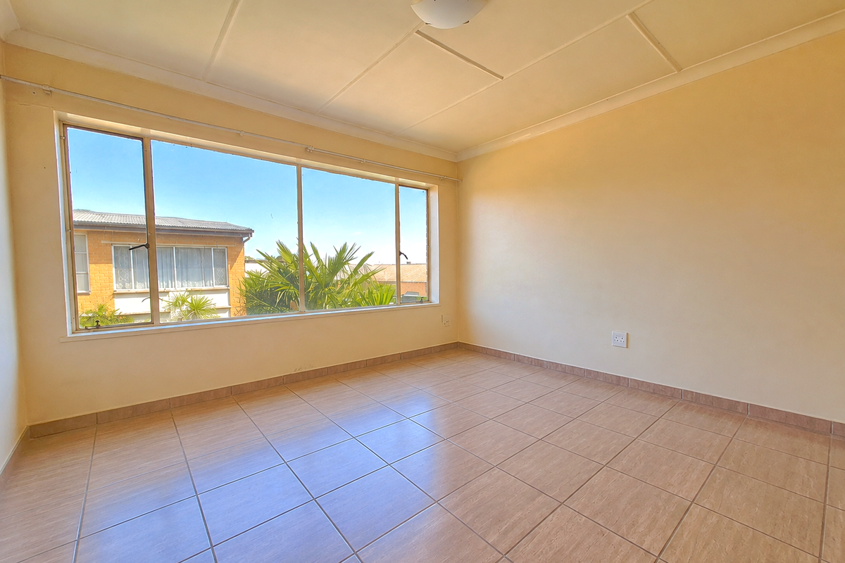 A bright, empty living room featuring large windows, tiled flooring, and neutral walls, offering a blank canvas for personalization.
