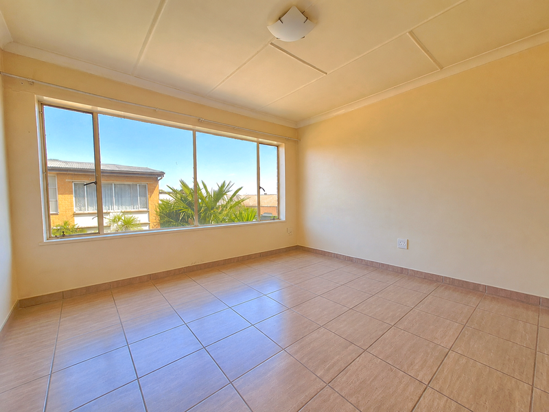 A bright, empty living room featuring large windows, tiled flooring, and neutral walls, offering a blank canvas for personalization.