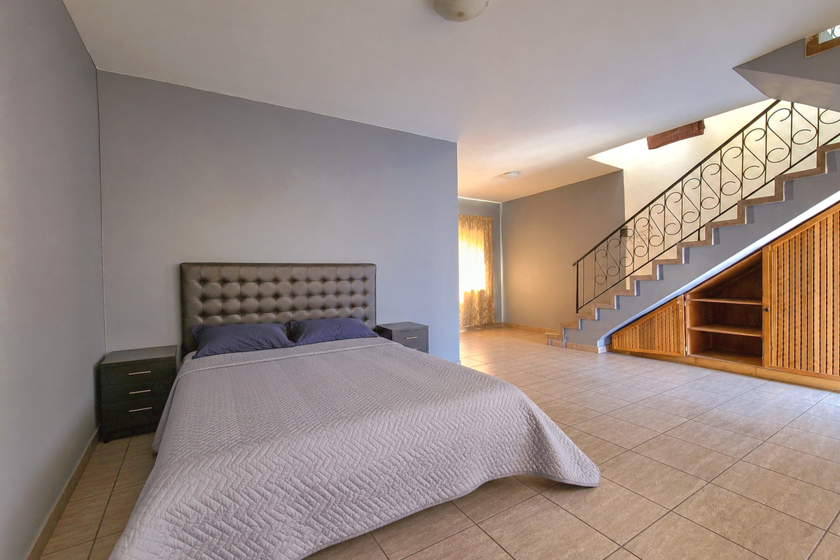 Spacious bedroom featuring tiled flooring, a staircase with decorative wrought iron railing, and convenient built-in under-stair storage cabinetry.