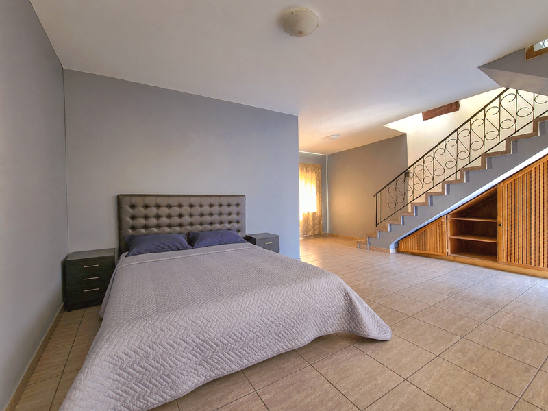 Spacious bedroom featuring tiled flooring, a staircase with decorative wrought iron railing, and convenient built-in under-stair storage cabinetry.