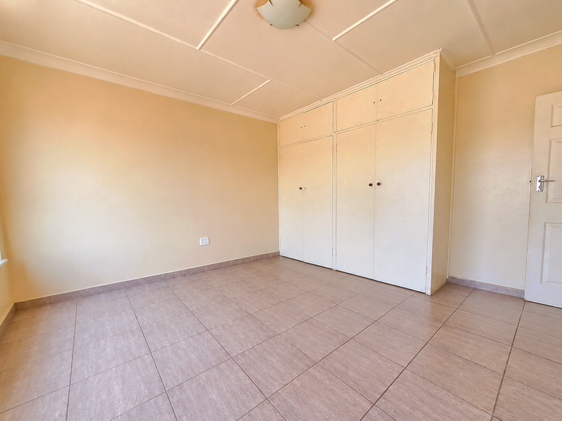A spacious, empty bedroom featuring neutral tiled flooring, built-in storage cupboards, and a standard panel door.