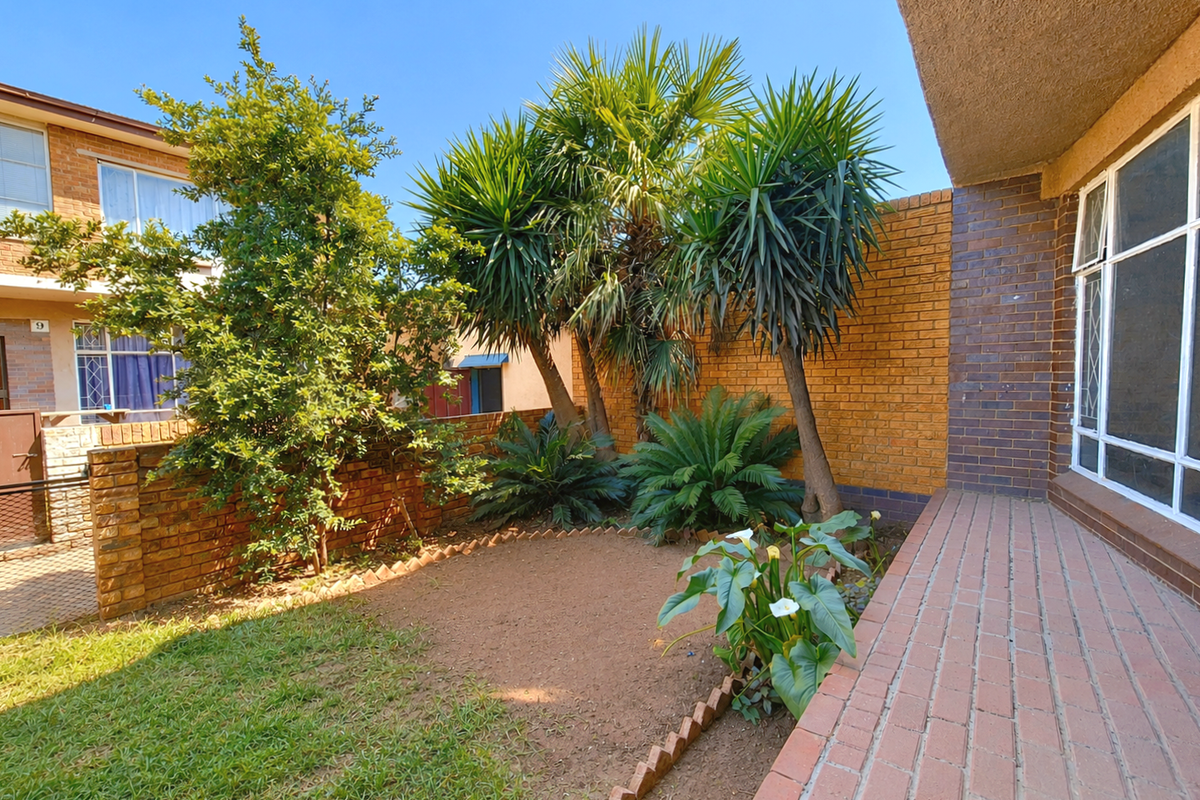 A private rear courtyard featuring a brick-paved patio, established garden beds, and a secure brick boundary wall.