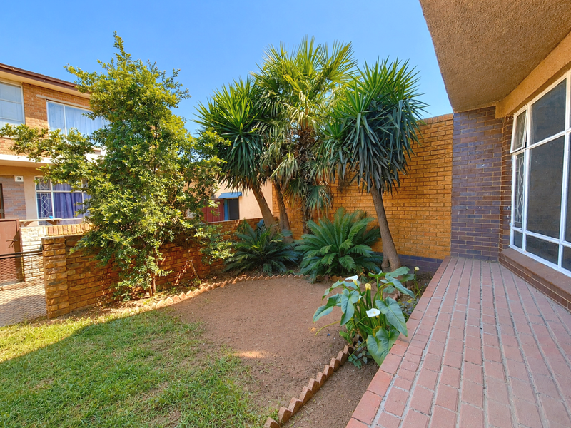 A private rear courtyard featuring a brick-paved patio, established garden beds, and a secure brick boundary wall.