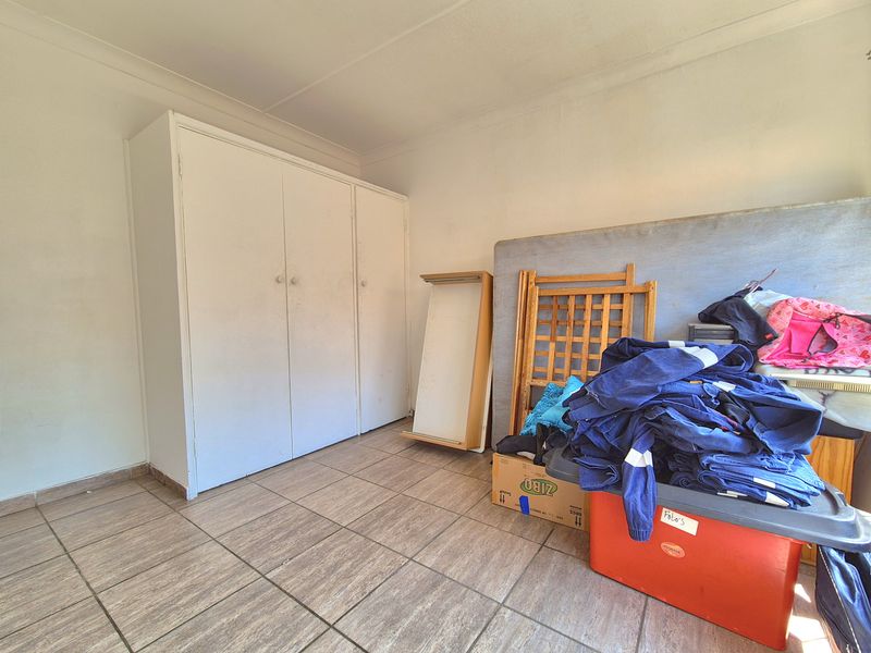 A bedroom featuring tiled flooring and a built-in wardrobe, currently used for storage. The space requires cosmetic updates to improve its overall condition.