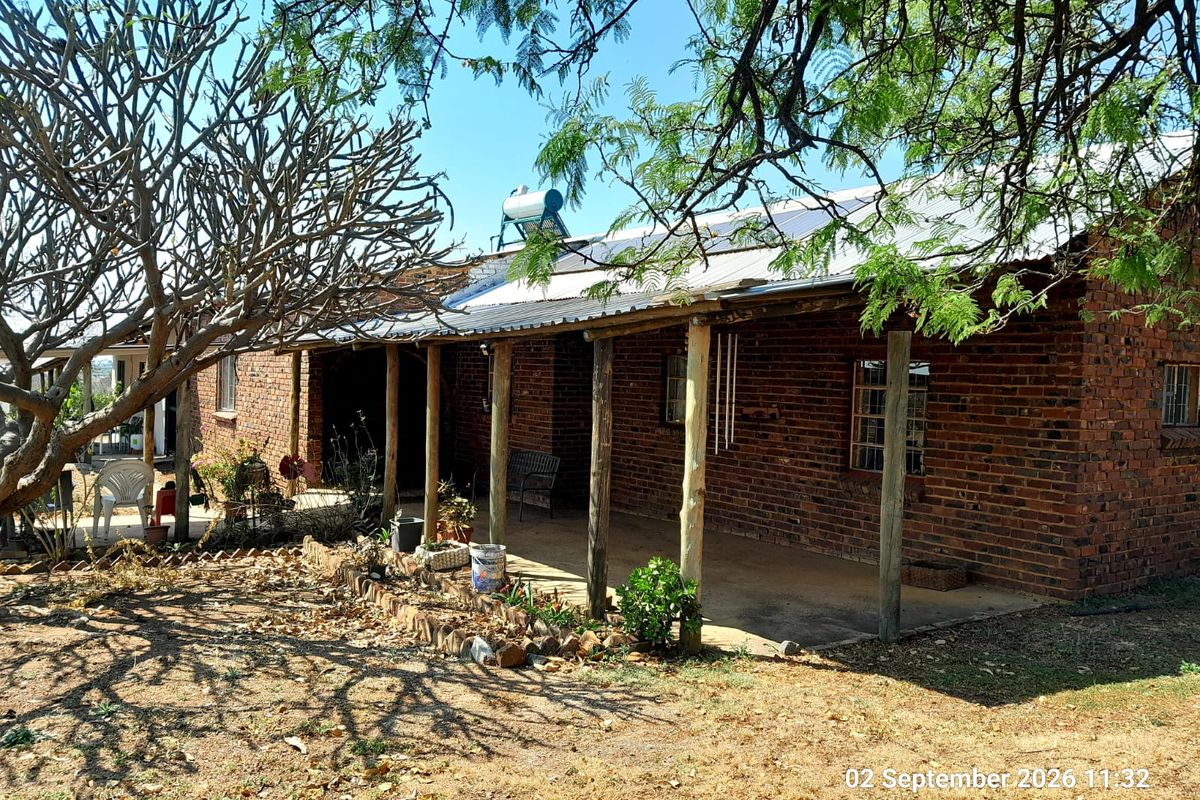 A rustic farmhouse exterior featuring exposed brick walls, a covered veranda with timber posts, and a roof-mounted solar water heating system.