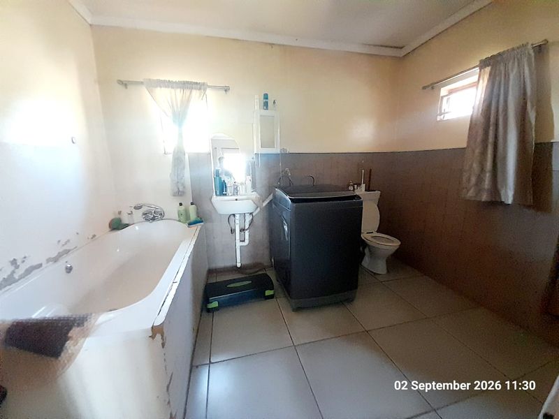 A functional bathroom featuring a bathtub, wall-mounted basin, and toilet, with tiled flooring and half-height wall tiling, requiring cosmetic updates.
