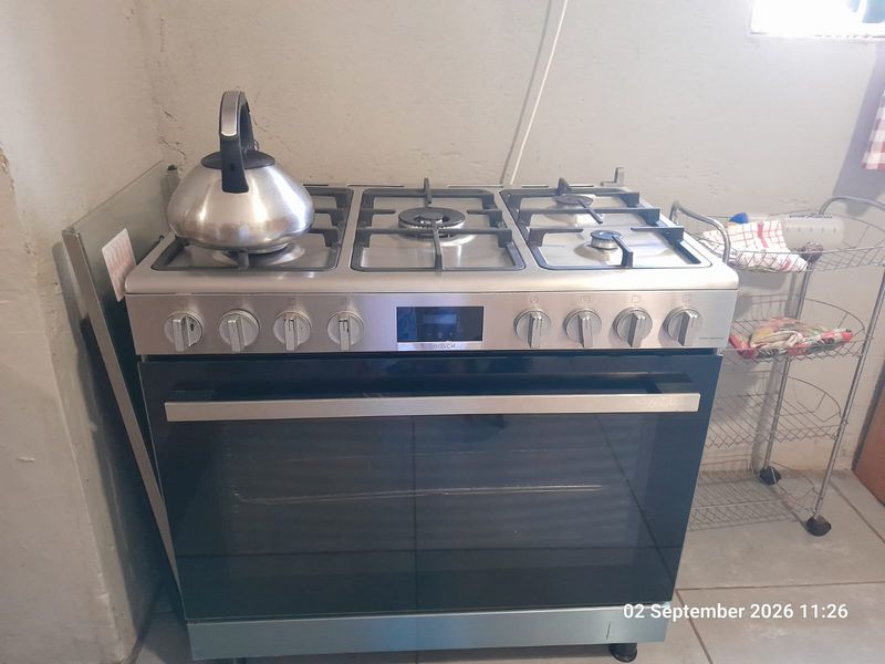 A kitchen area featuring a stainless steel freestanding gas stove and oven, set against unfinished plaster walls with visible wiring.