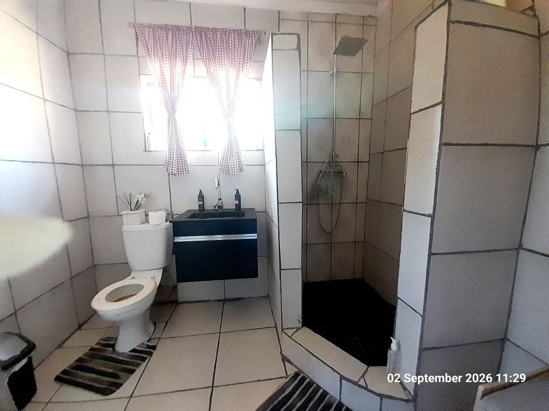 A functional bathroom featuring a walk-in shower, wall-mounted vanity, and toilet, finished with tiled walls and flooring throughout.