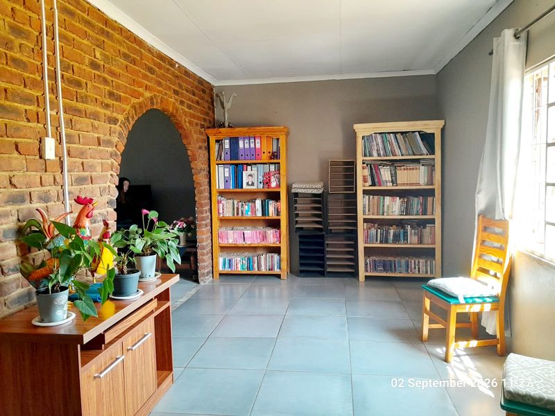 A living area featuring an exposed brick wall with an arched opening, tiled flooring, and natural light from a side window.