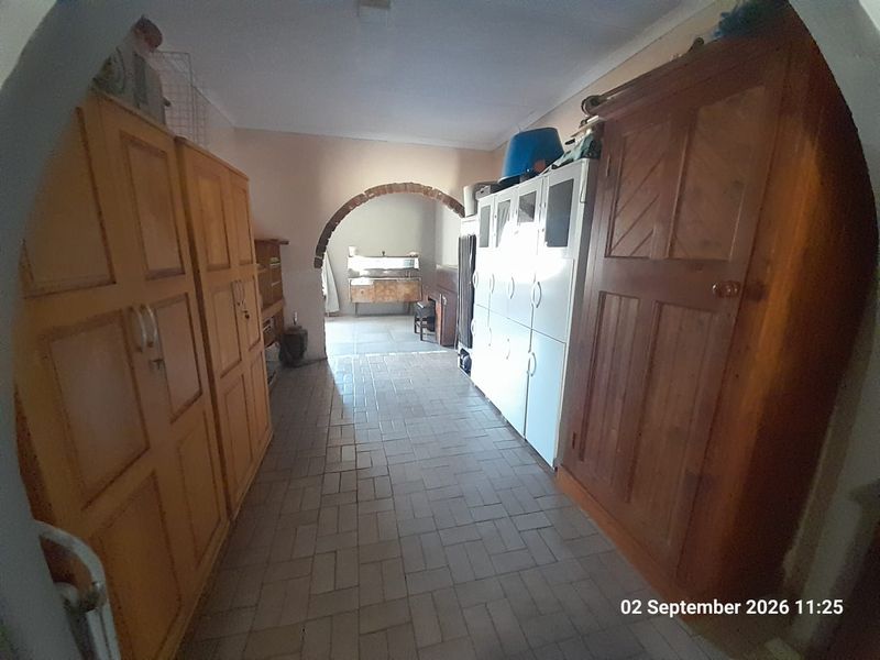 A hallway featuring tiled flooring and a distinctive brick archway leading to an adjacent room, with built-in storage cabinetry along the walls.