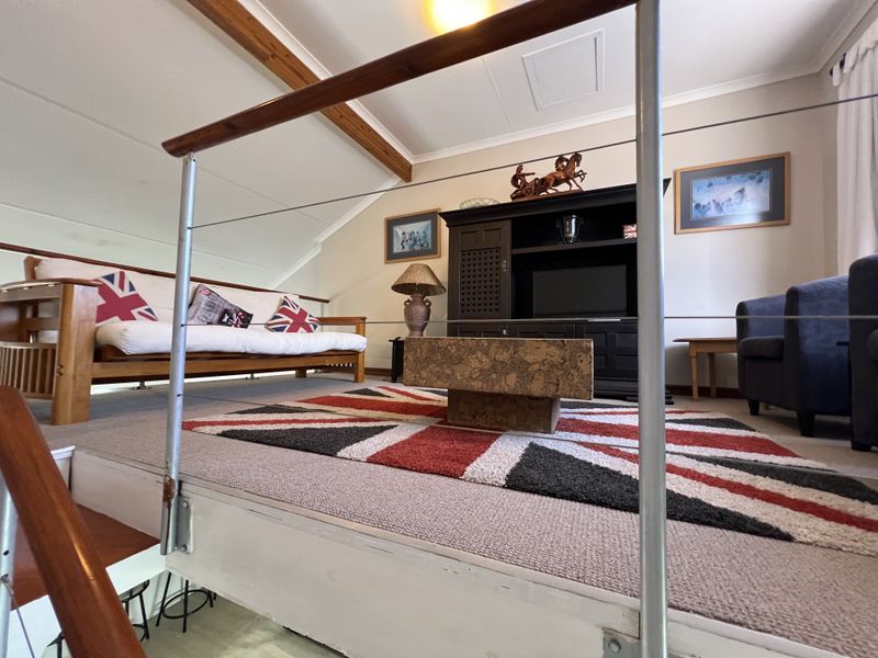 A loft-style living area featuring exposed timber ceiling beams, carpeted flooring, and a metal staircase railing with visible signs of wear.