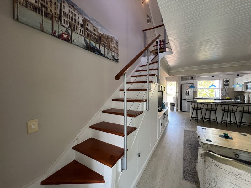 Open plan living area featuring a timber staircase with integrated storage, leading to a modern kitchen with a breakfast island and light wood-look flooring.