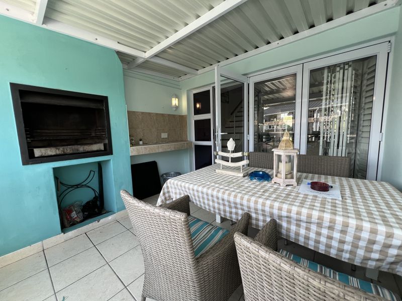 Covered patio area featuring a built-in braai, tiled prep counter, and direct access to the interior through sliding glass doors.