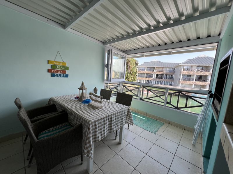 Covered balcony featuring a built-in braai, tiled flooring, and folding glass doors, offering an outdoor dining space with views of the complex.