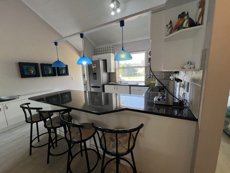 Open-plan kitchen featuring a granite breakfast bar, modern pendant lighting, and ample built-in cabinetry, creating a functional and connected living space.