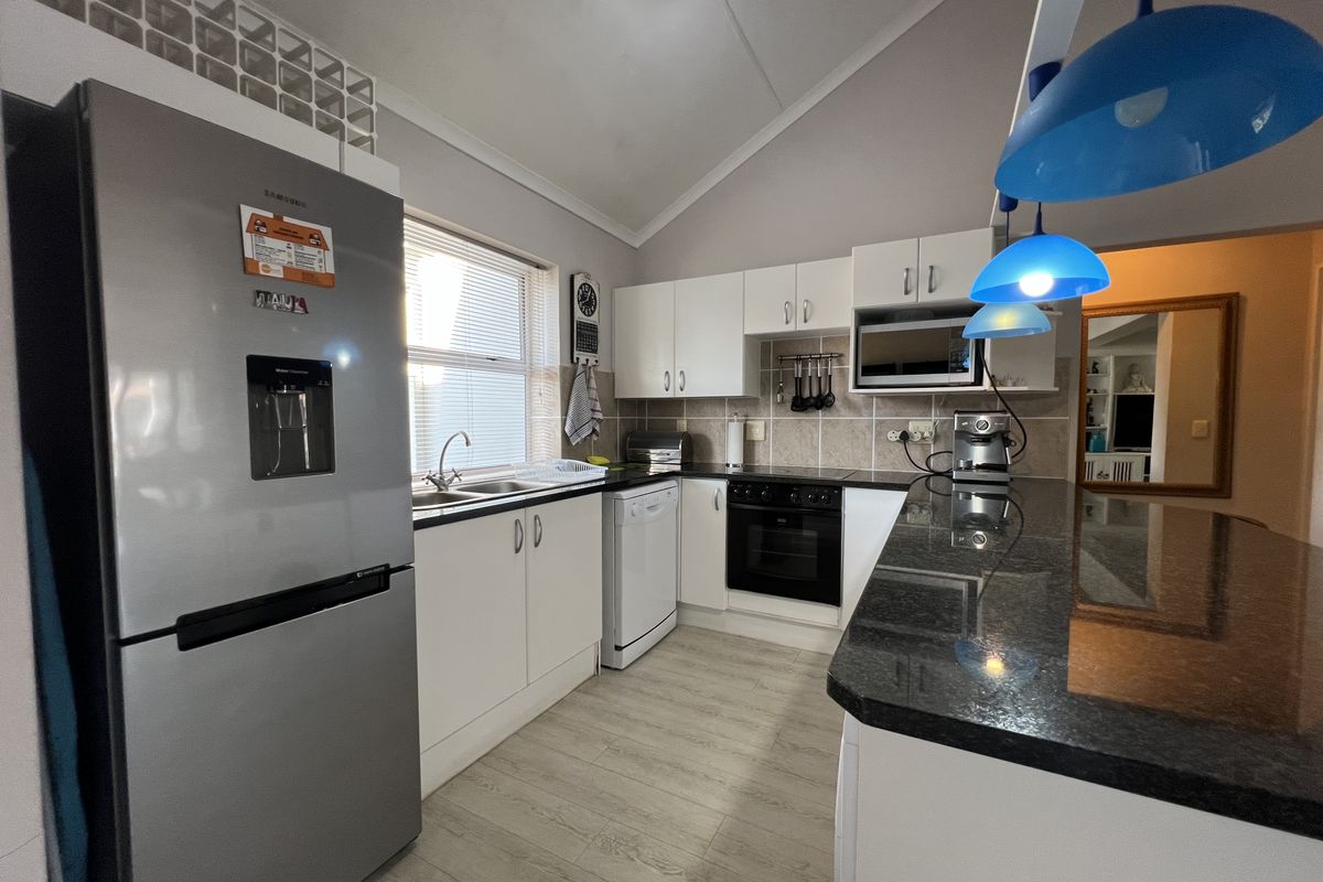 Modern kitchen featuring granite countertops, built-in oven and hob, ample cabinetry, and a breakfast bar, finished with light laminate flooring and a tiled backsplash.