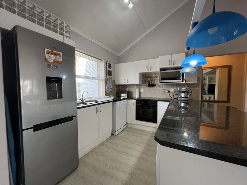 Modern kitchen featuring granite countertops, built-in oven and hob, ample cabinetry, and a breakfast bar, finished with light laminate flooring and a tiled backsplash.