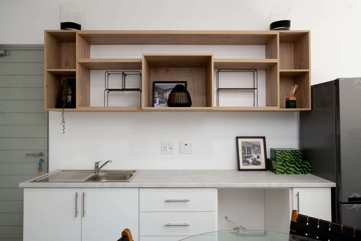 A modern kitchen area featuring white cabinetry, a stainless steel sink, and extensive open wooden shelving for storage.