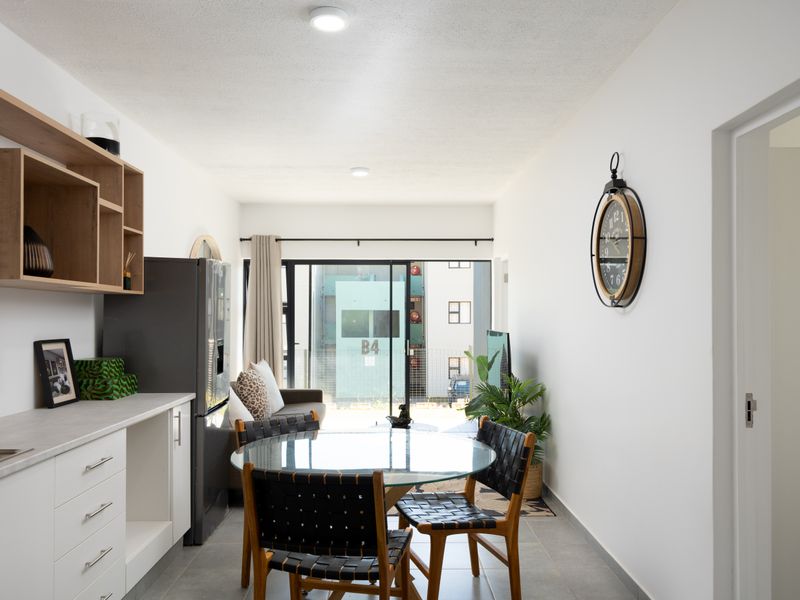 A bright open-plan living and dining area featuring modern white cabinetry, tiled flooring, and large sliding glass doors leading to an outdoor space.