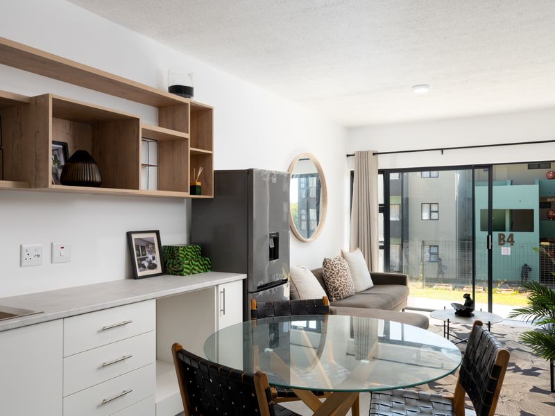 Modern open-plan living area featuring a compact kitchen with built-in cabinetry, shelving, and large sliding glass doors leading to an outdoor space.