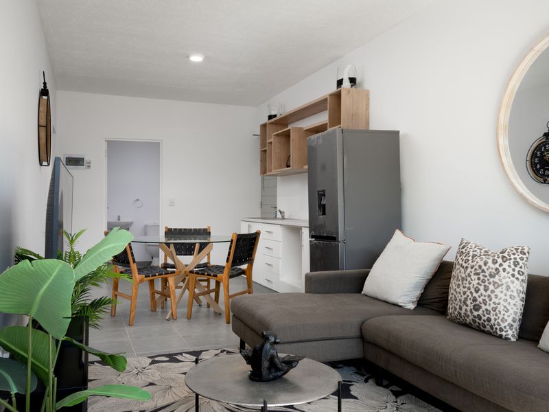 Open-plan living area featuring a compact kitchen with built-in cabinetry and tiled flooring, seamlessly flowing into the dining and lounge space.
