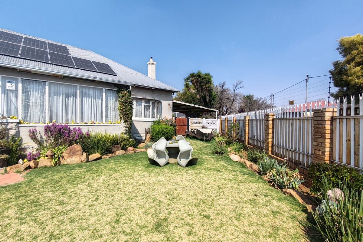 Rear garden area featuring a well-maintained lawn, brick boundary wall with metal fencing, and solar panels installed on the roof.