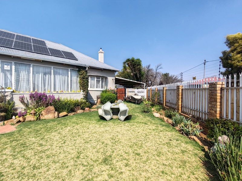 Rear garden area featuring a well-maintained lawn, brick boundary wall with metal fencing, and solar panels installed on the roof.