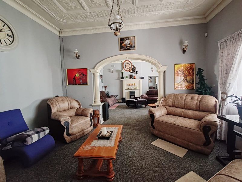 A spacious living room featuring an ornate plaster ceiling, a decorative archway leading to an adjoining area, and a traditional fireplace.