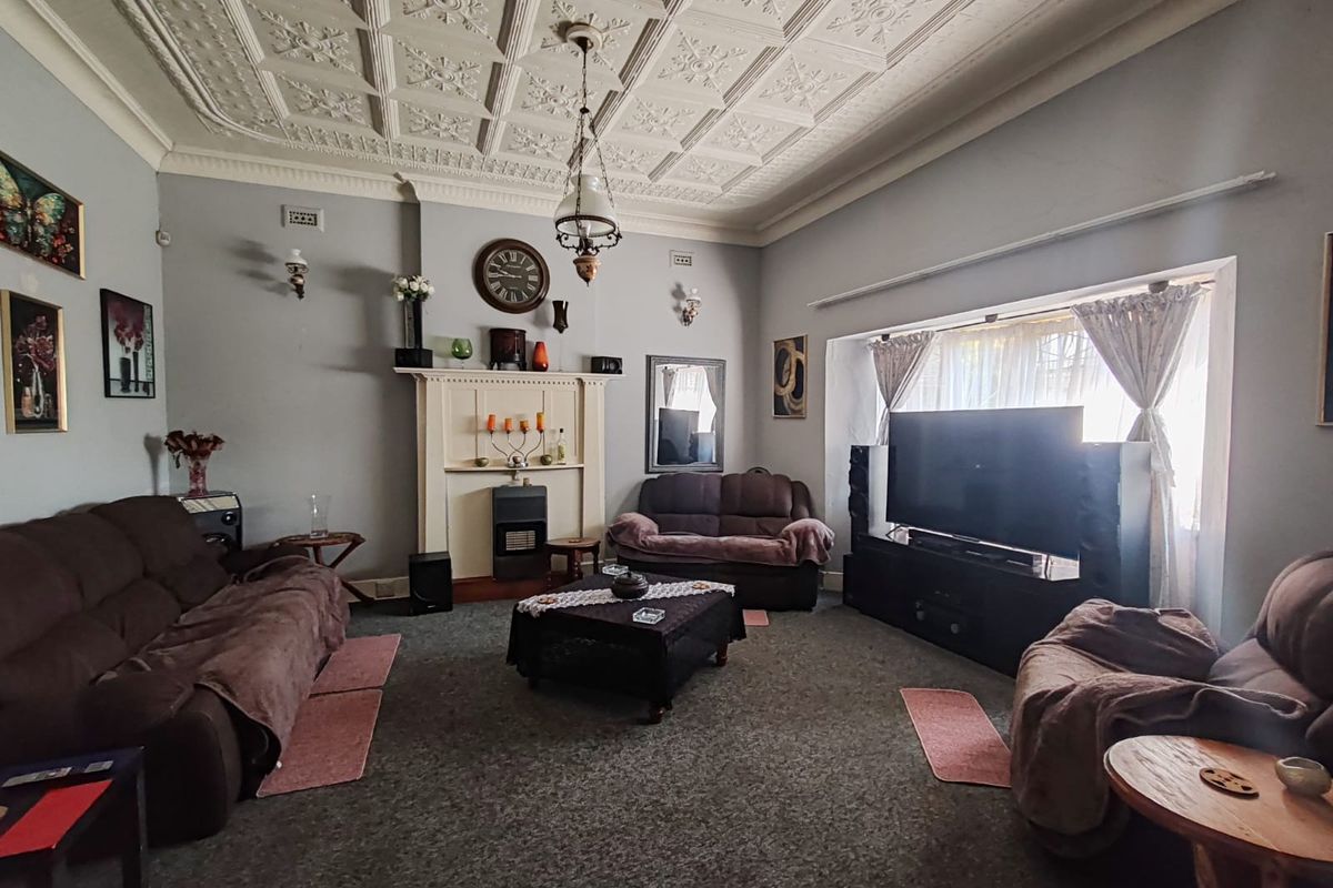 Spacious living room featuring a classic ornate pressed metal ceiling, fireplace mantel with built-in heater, and large window providing natural light.