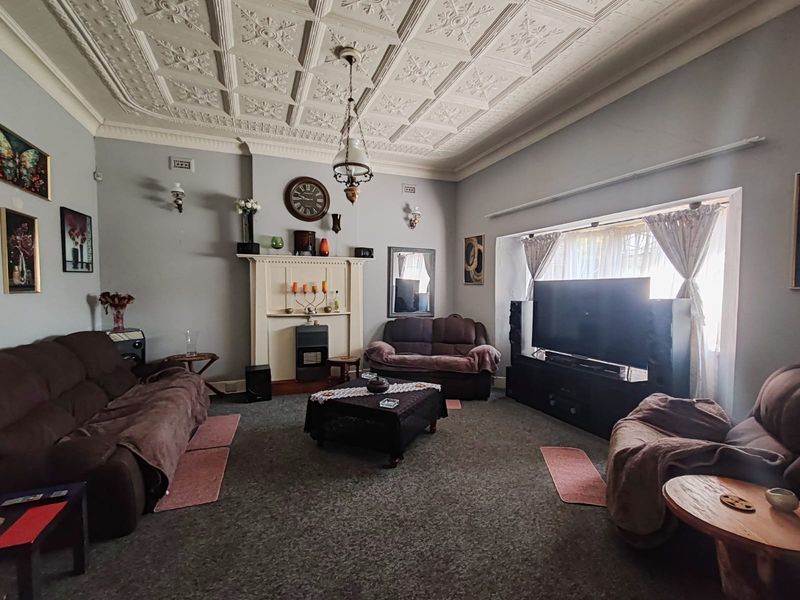 Spacious living room featuring a classic ornate pressed metal ceiling, fireplace mantel with built-in heater, and large window providing natural light.