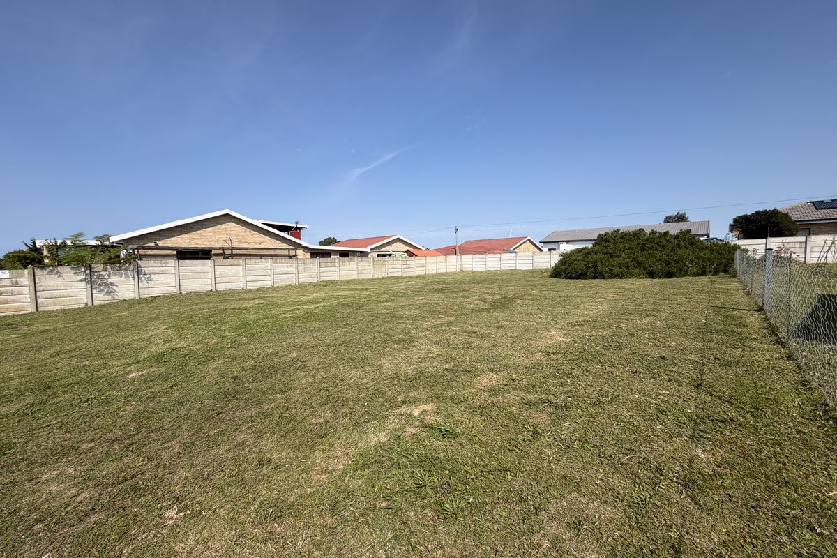 A vacant residential plot featuring a level lawn, enclosed by a precast concrete boundary wall and chain link fencing.