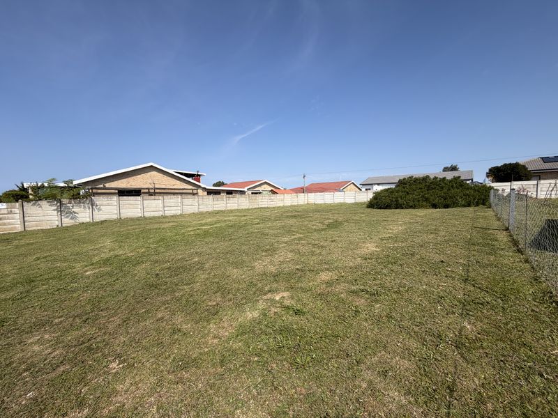 A vacant residential plot featuring a level lawn, enclosed by a precast concrete boundary wall and chain link fencing.