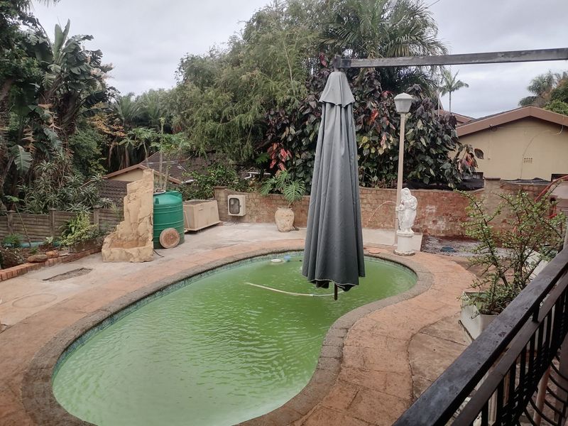 Outdoor pool area featuring a paved surround, brick boundary walls, and a water tank, currently requiring maintenance and pool water treatment.