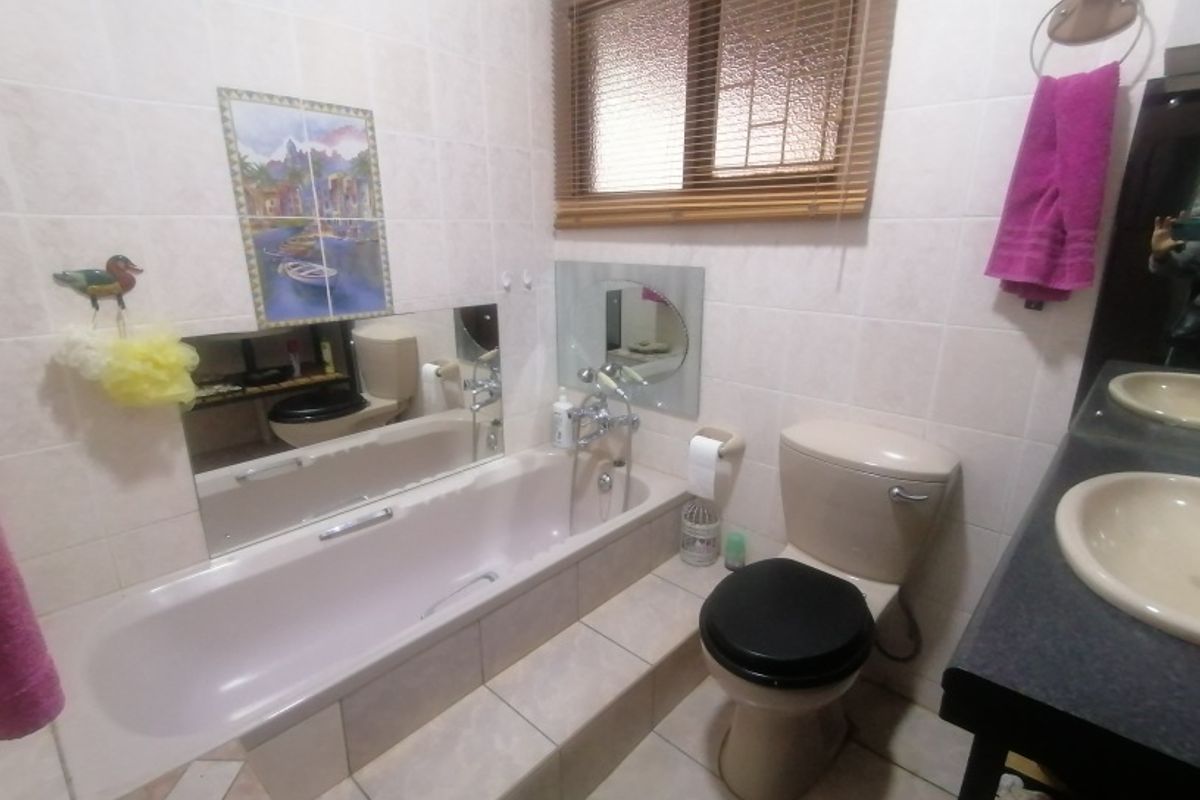 A functional bathroom featuring a built-in bathtub, dual vanity basins, and tiled finishes. The space offers a practical layout with natural light.