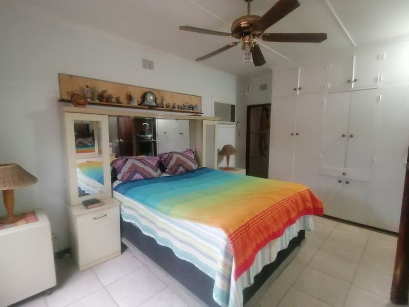 A bedroom featuring built-in cupboards, tiled flooring, a ceiling fan, and an integrated air conditioning unit.