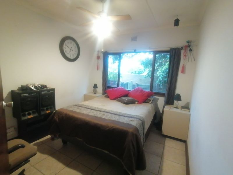 A functional bedroom featuring tiled flooring, a ceiling fan, and a large window providing natural light.