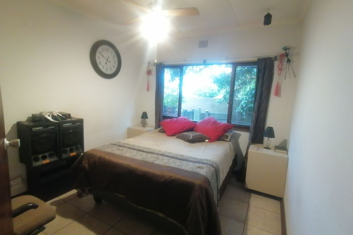 A functional bedroom featuring tiled flooring, a ceiling fan, and a large window providing natural light.