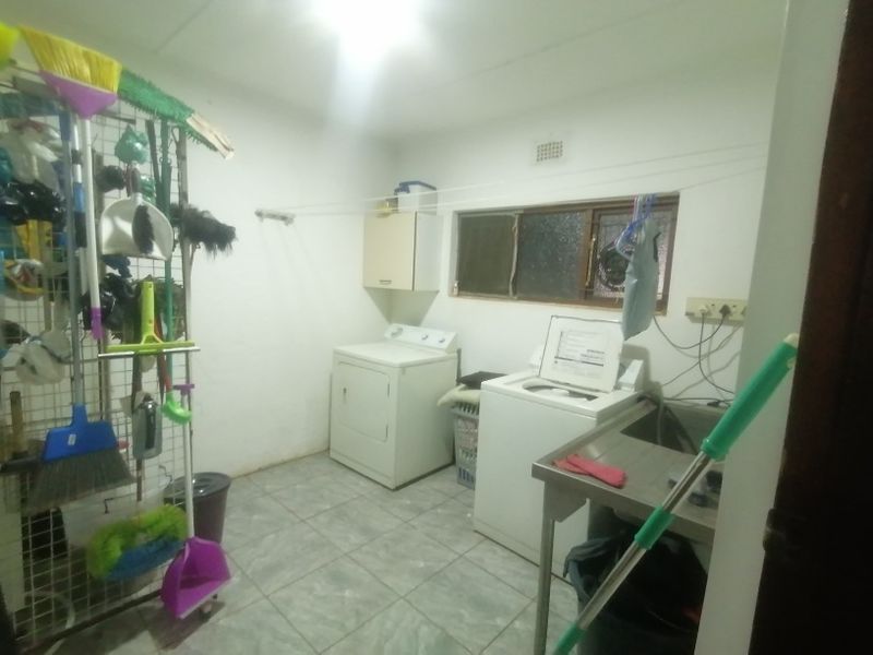 A functional laundry room featuring tiled floors, a stainless steel utility sink, wall-mounted storage cabinetry, and a built-in drying rack.