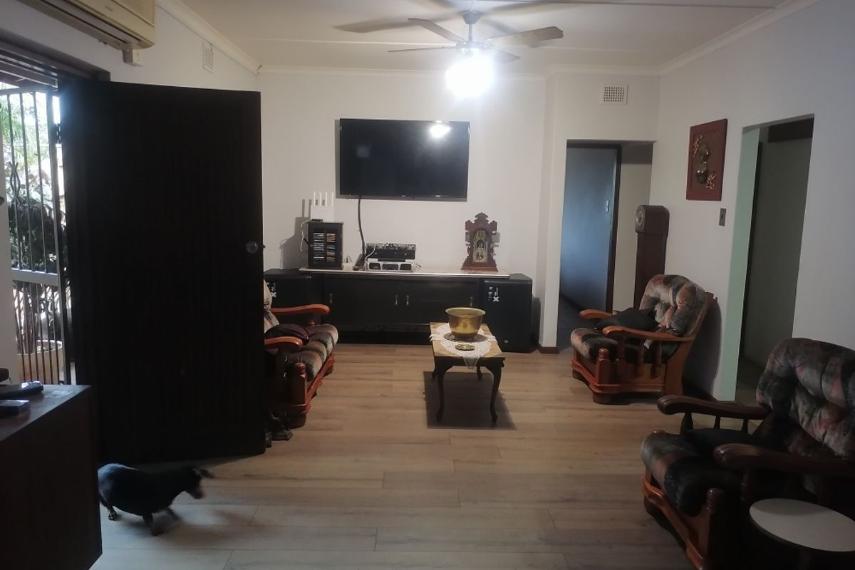 A living room featuring laminate flooring, a ceiling fan, and a wall-mounted air conditioning unit.
