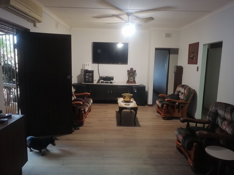 A living room featuring laminate flooring, a ceiling fan, and a wall-mounted air conditioning unit.