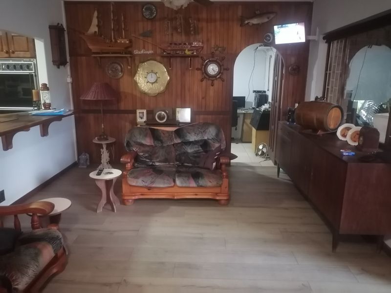 Living room featuring wood paneling, an arched doorway, and modern laminate flooring, with an adjacent kitchen area visible.