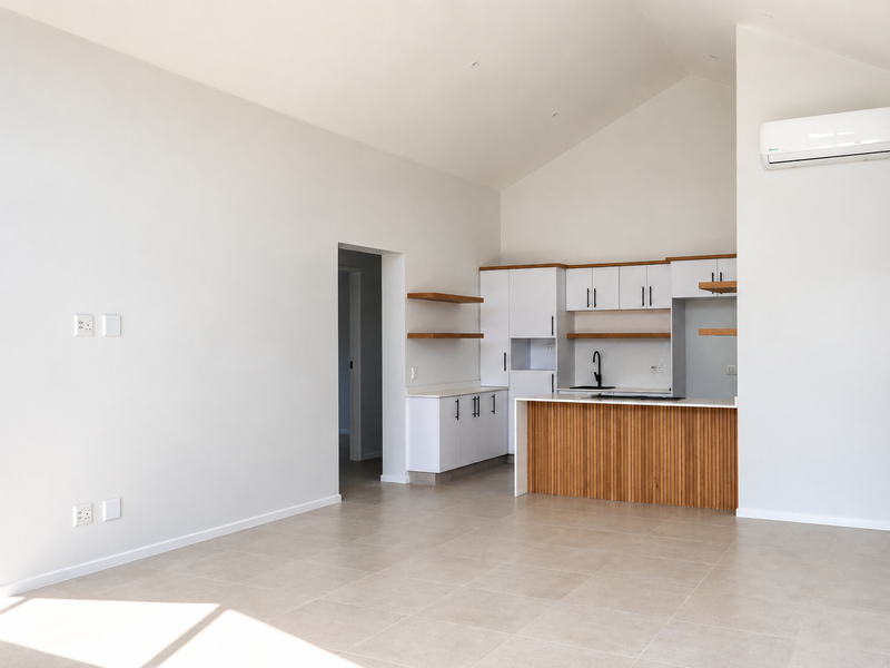 Modern open-plan living area featuring a contemporary kitchen with timber-accented island, tiled flooring, vaulted ceilings, and a wall-mounted air conditioning unit.