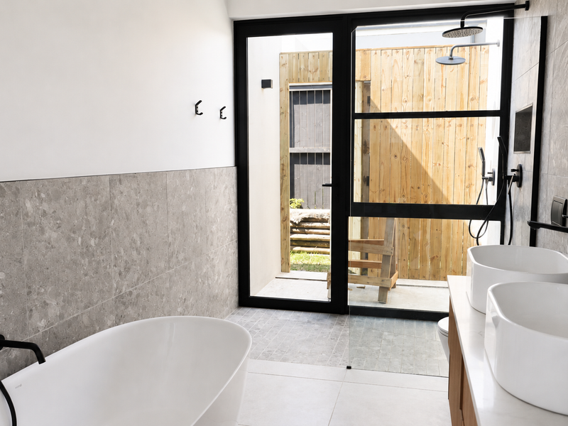Modern bathroom featuring a freestanding bathtub, double vanity with vessel sinks, black matte fixtures, and a glass door leading to a private outdoor area.
