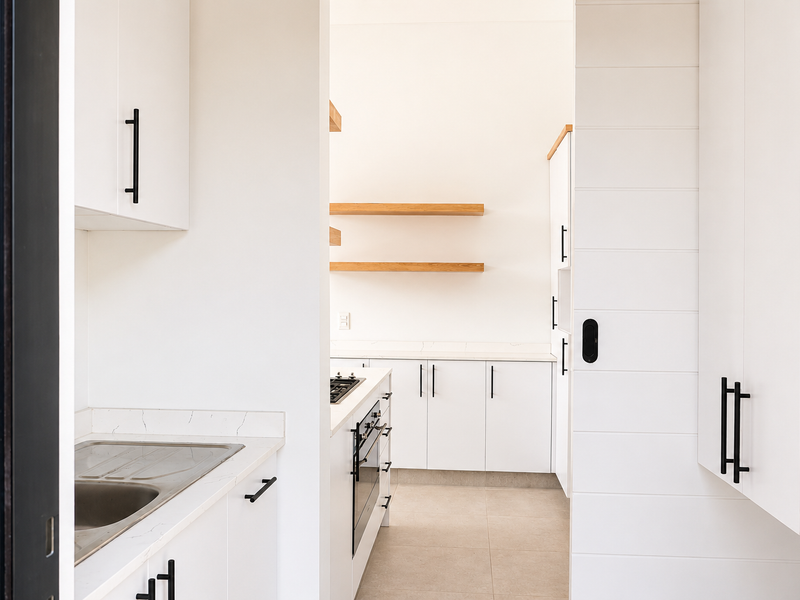 Modern kitchen featuring white cabinetry, stone countertops, integrated appliances, and floating timber shelving in a clean, minimalist design.