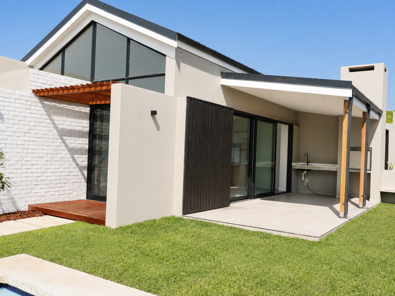 Modern rear exterior featuring a covered patio with built-in braai, outdoor sink, timber decking, and large sliding glass doors overlooking the garden.