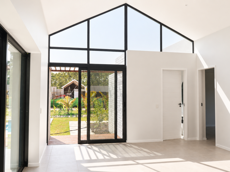 Bright and spacious living area featuring a high vaulted ceiling, large black-framed windows, and direct access to the outdoor patio and garden.