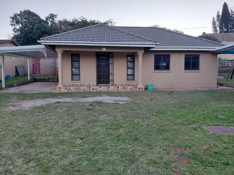 Front view of a single-story flat featuring a tiled roof, covered porch with stone cladding, and an attached carport.