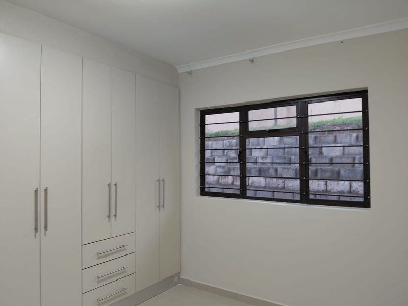A clean, empty bedroom featuring neutral walls, tiled flooring, and ample built-in cupboard storage with modern hardware.