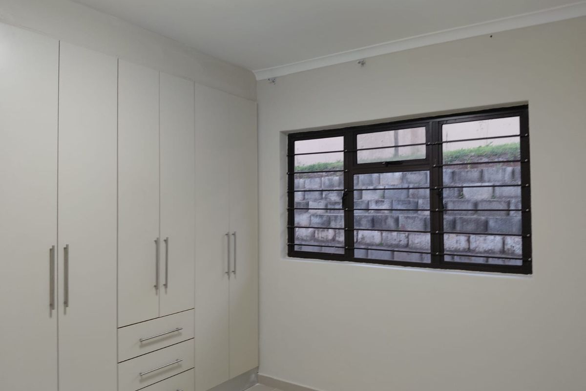 A clean, empty bedroom featuring neutral walls, tiled flooring, and ample built-in cupboard storage with modern hardware.