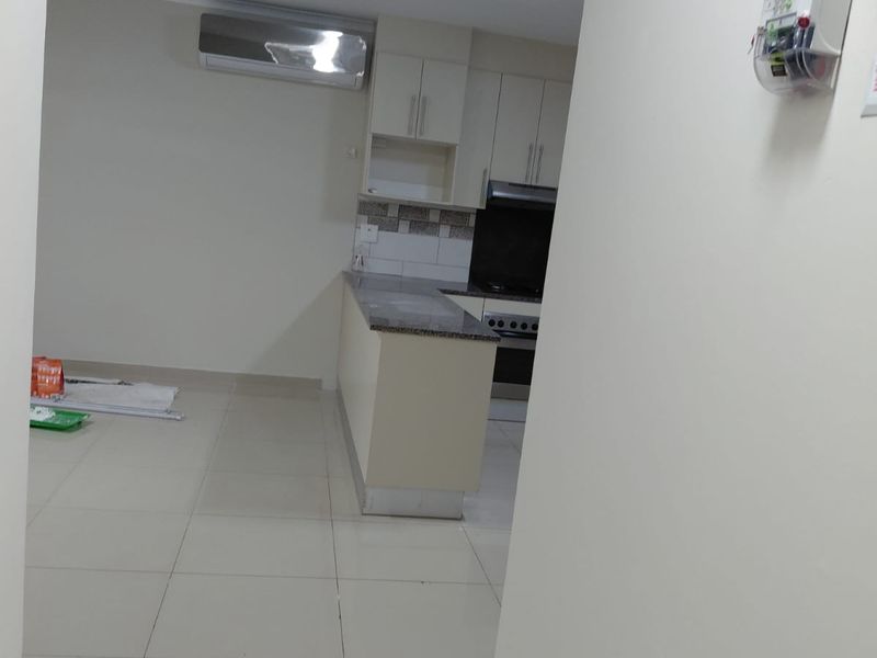 An open-plan kitchen area featuring tiled flooring, built-in cabinetry with granite countertops, an integrated oven, and a wall-mounted air conditioning unit.
